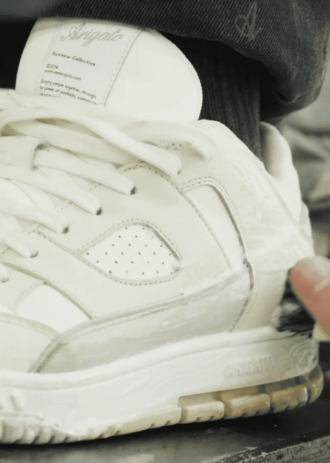 Close-up of a person wearing white sneakers with visible branding on the tongue and sole, adjusting the shoe with their hand.