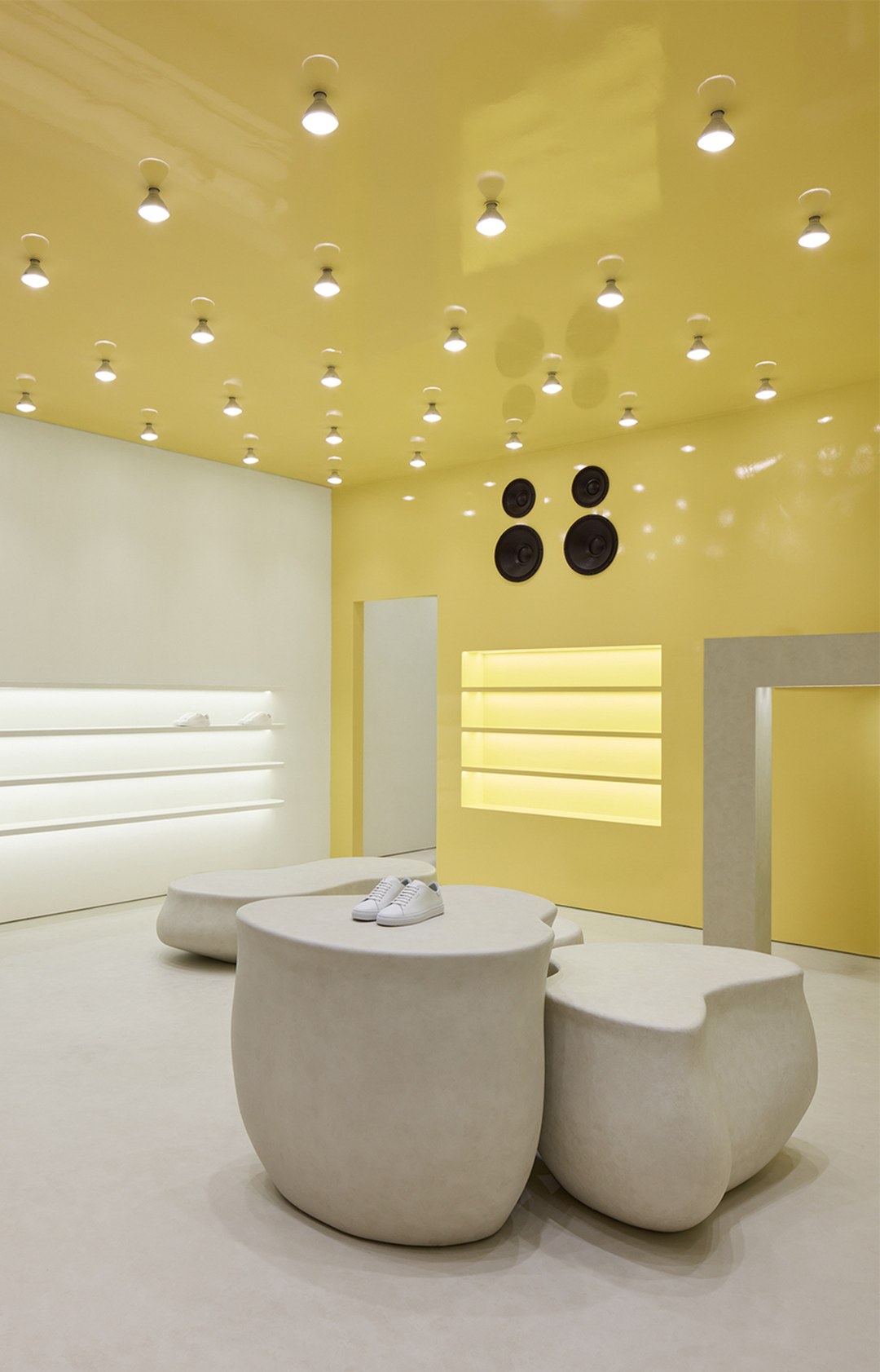 Modern interior with yellow ceiling, white walls, and minimalist stone furniture. Shelves with soft lighting and ceiling lights enhance the space.