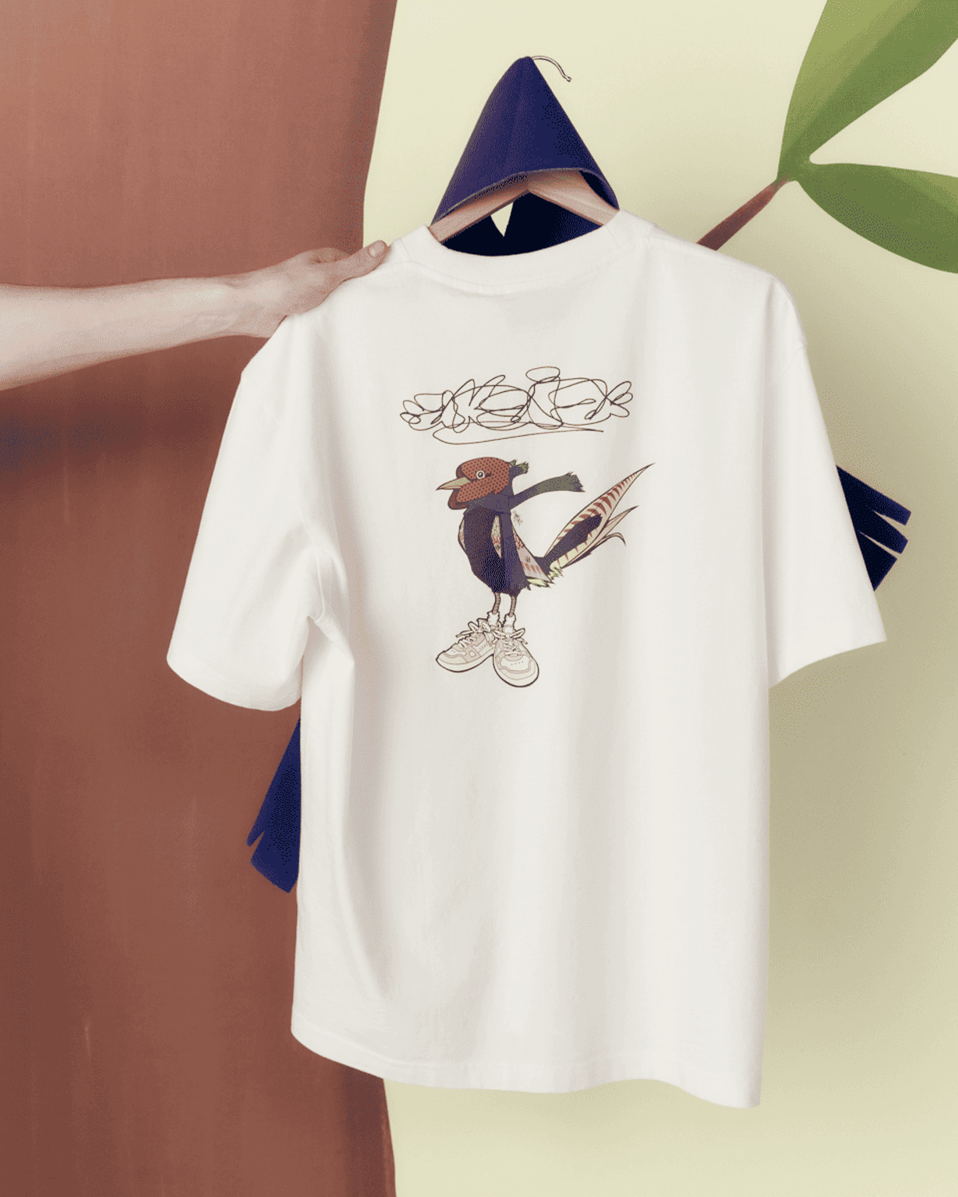 White T-shirt hanging, featuring a cartoon bird wearing sneakers. Background includes abstract shapes and a hand holding the hanger.