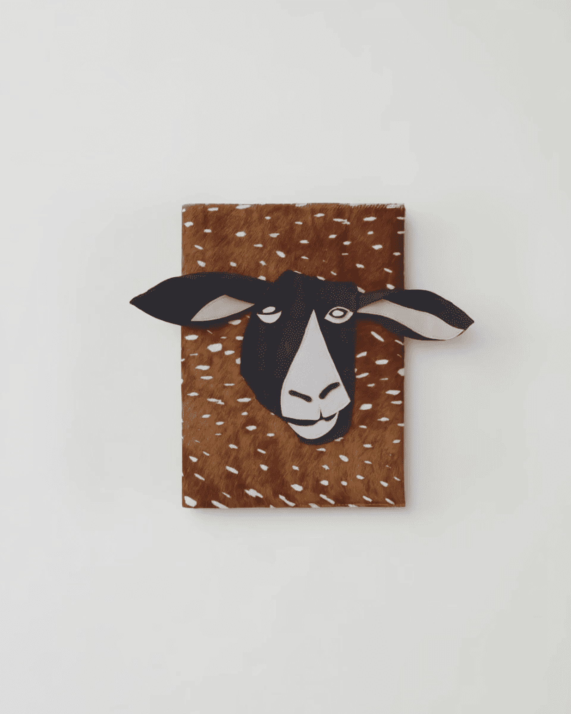 A rectangular object with a brown, spotted surface and a 3D illustration of a goat's head extending from it, against a white background.