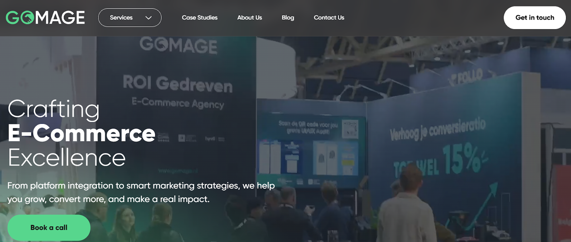 Exhibition booth with "GOMAGE" branding, showcasing e-commerce services with large screens and attendees engaging with displays.