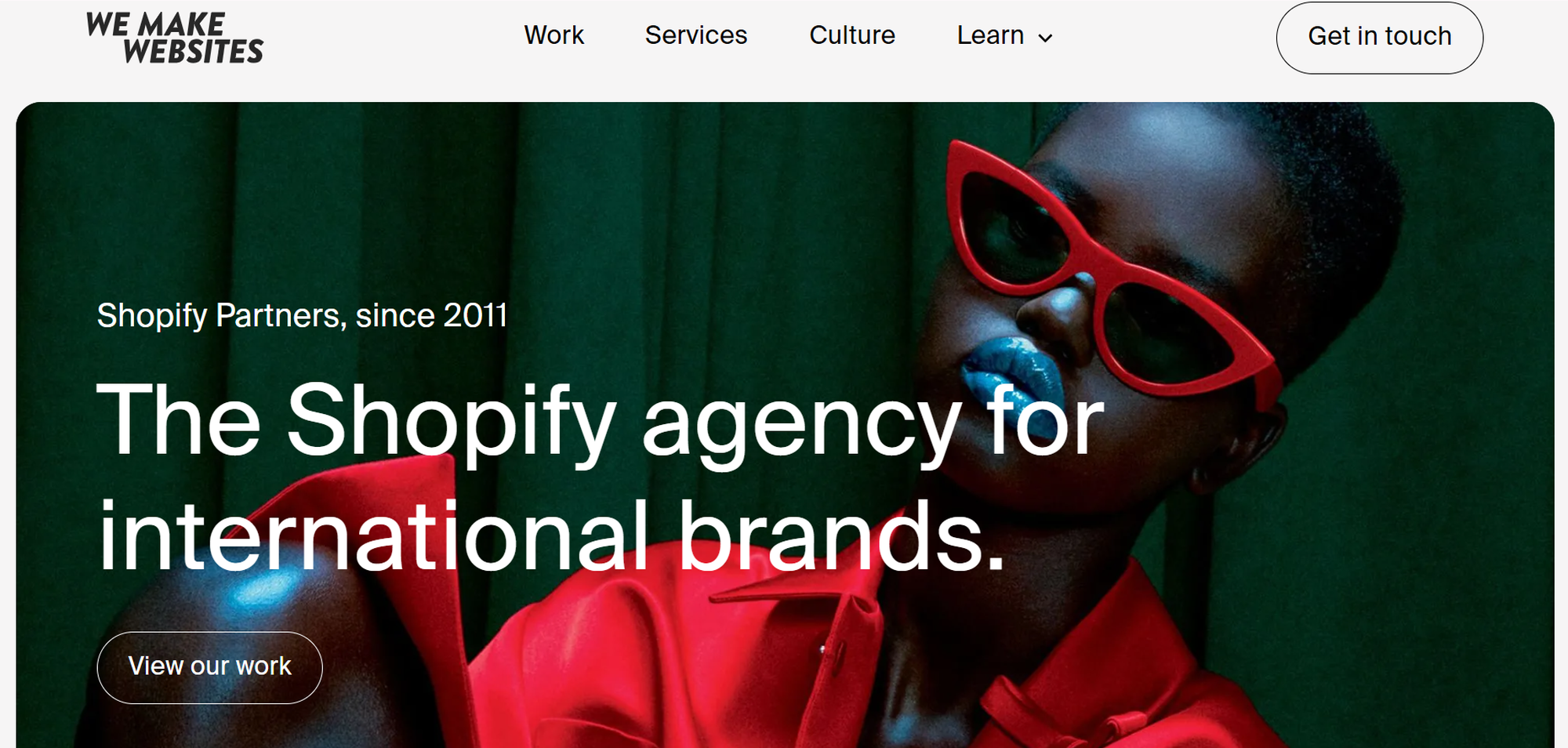 Fashionable person in red sunglasses and outfit against a green background. Text: "The Shopify agency for international brands."
