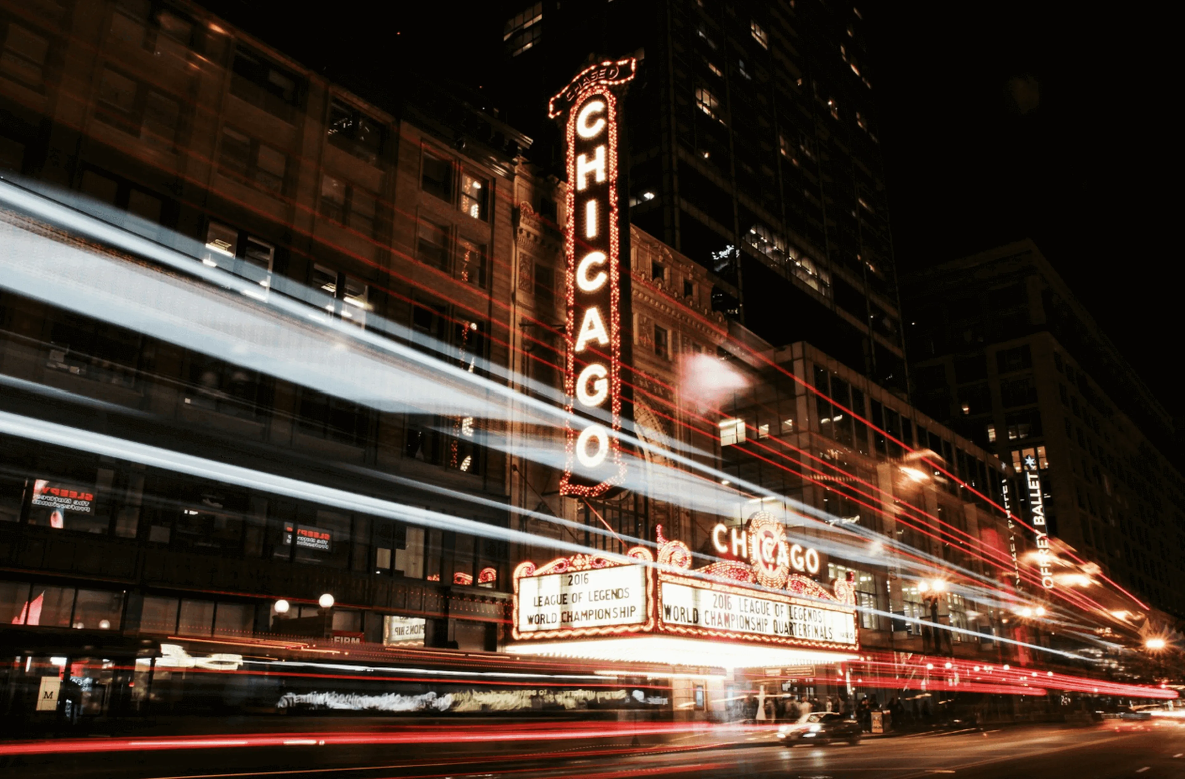 Night view of the iconic Chicago Theater with bright marquee lights and blurred light trails from passing traffic.