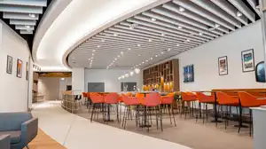Modern lounge with curved ceiling, orange chairs, and a bar area. Pendant lights hang above tables, and framed art decorates the walls.