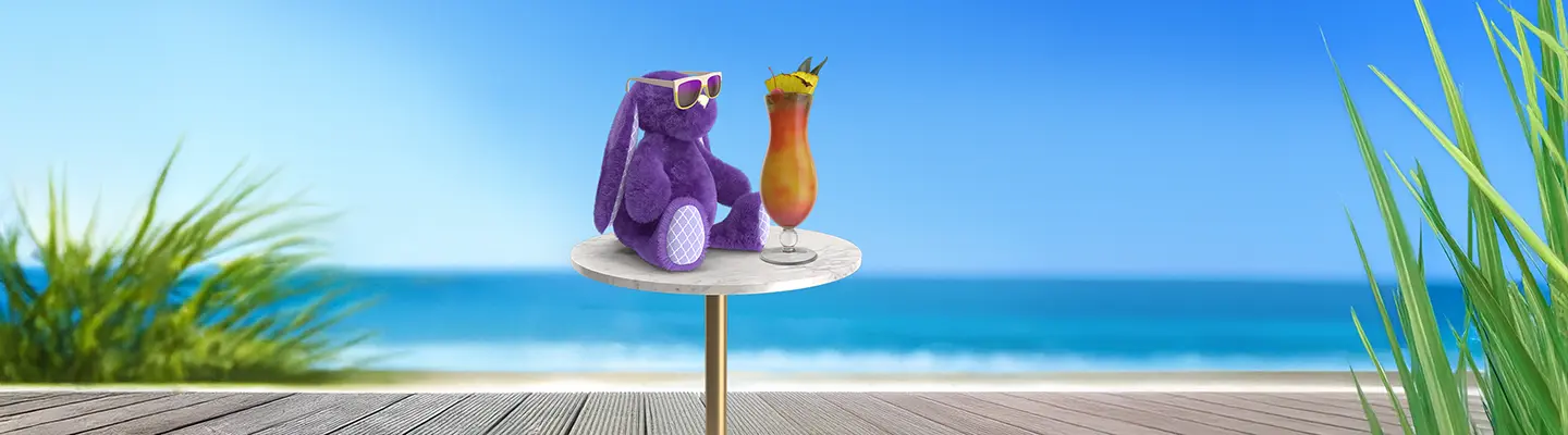 Purple plush bunny with sunglasses sits beside a colorful cocktail on a small table, overlooking a sunny beach and ocean.