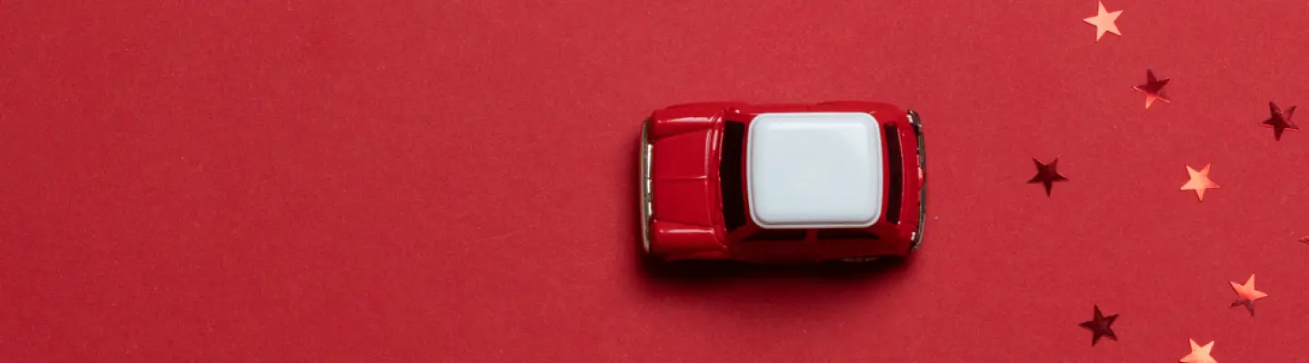 Toy red car with a white top on a red background, surrounded by scattered star-shaped confetti.