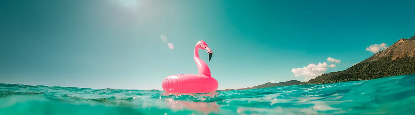Pink flamingo float on turquoise water against a clear blue sky, with distant mountains and clouds on the horizon.