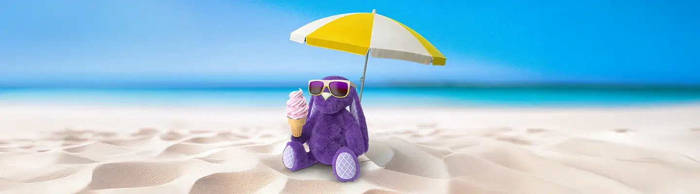 Purple plush dinosaur with sunglasses holds an ice cream cone under a yellow and white beach umbrella on sandy beach with blue ocean background.