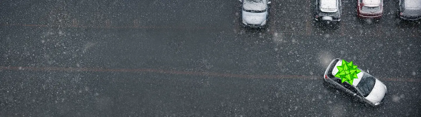 Aerial view of a snowy parking lot; cars parked at top, one car at right with a large green gift bow on its roof.