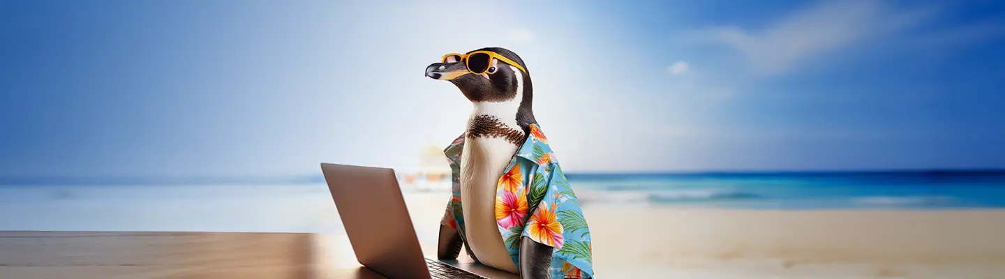A penguin in sunglasses and a floral shirt sits at a laptop on a beach, with the ocean and sky in the background.