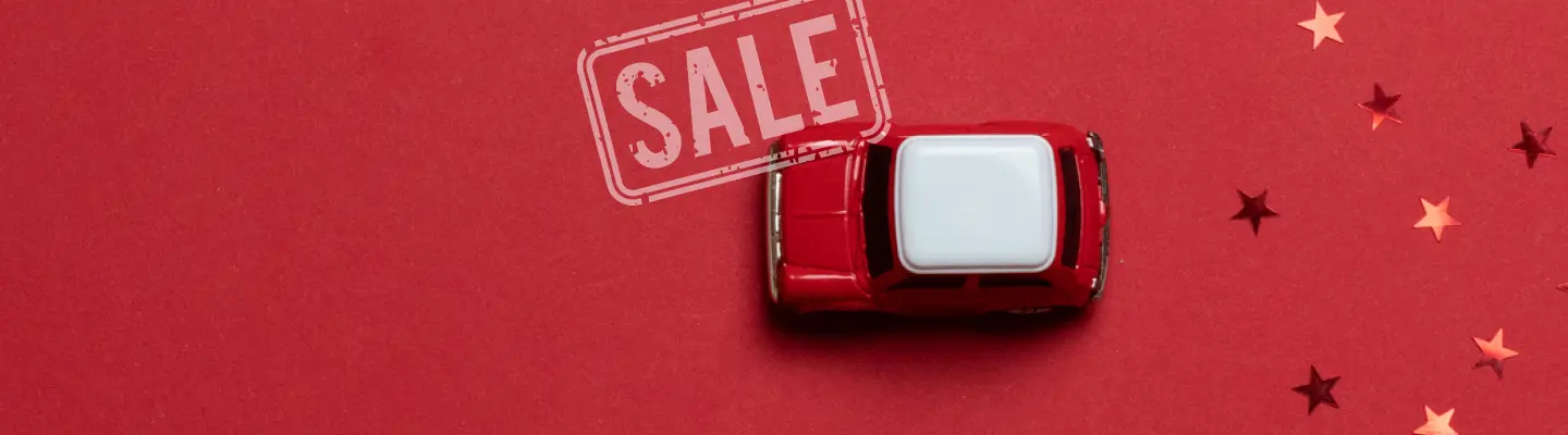Red toy car on a red surface with scattered star confetti and a "SALE" stamp above.