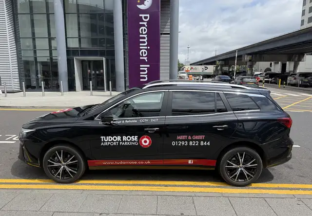 Black Tudor Rose Airport Parking car parked outside Premier Inn with signage and contact details.