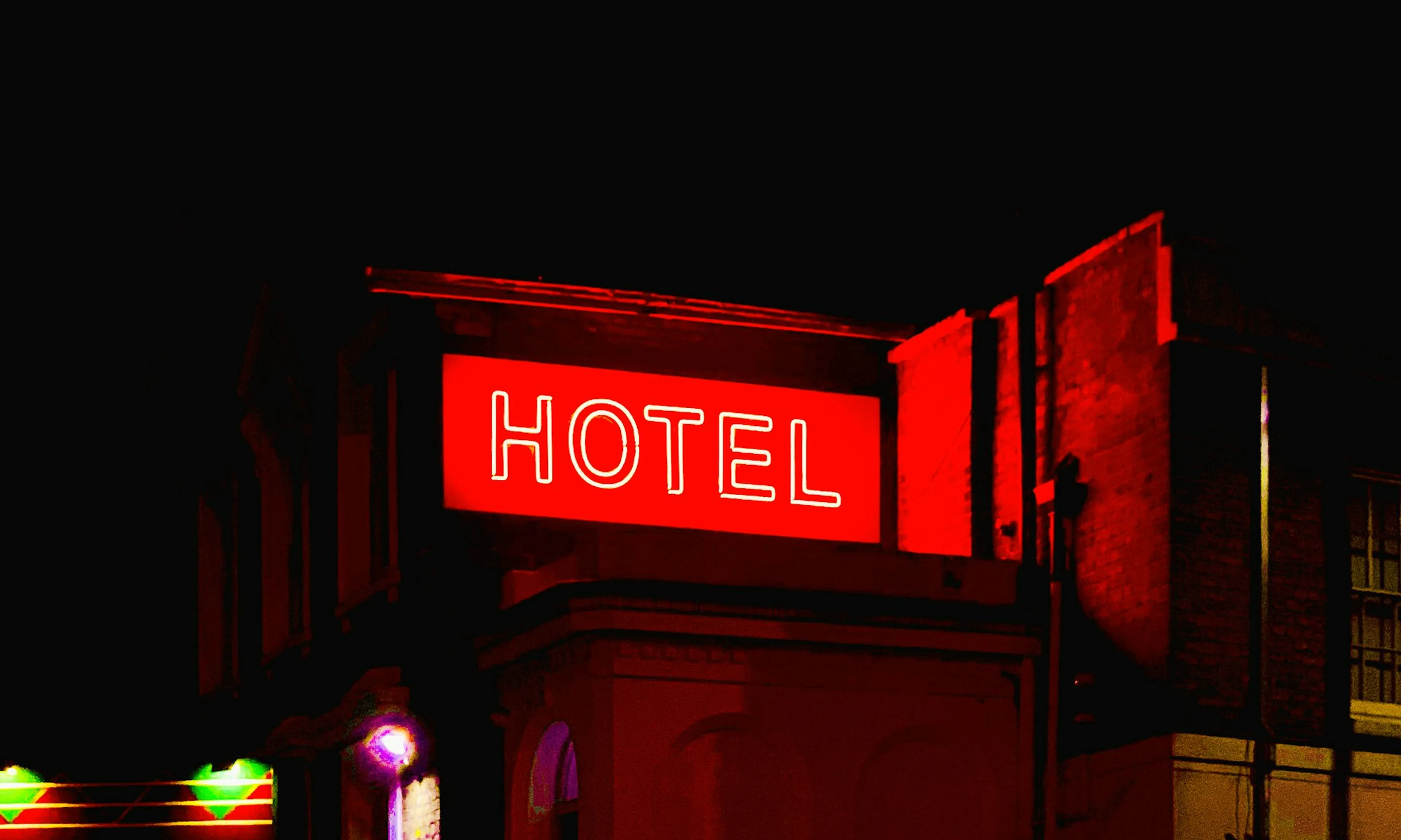 Red neon "HOTEL" sign glowing on a dark building facade at night.