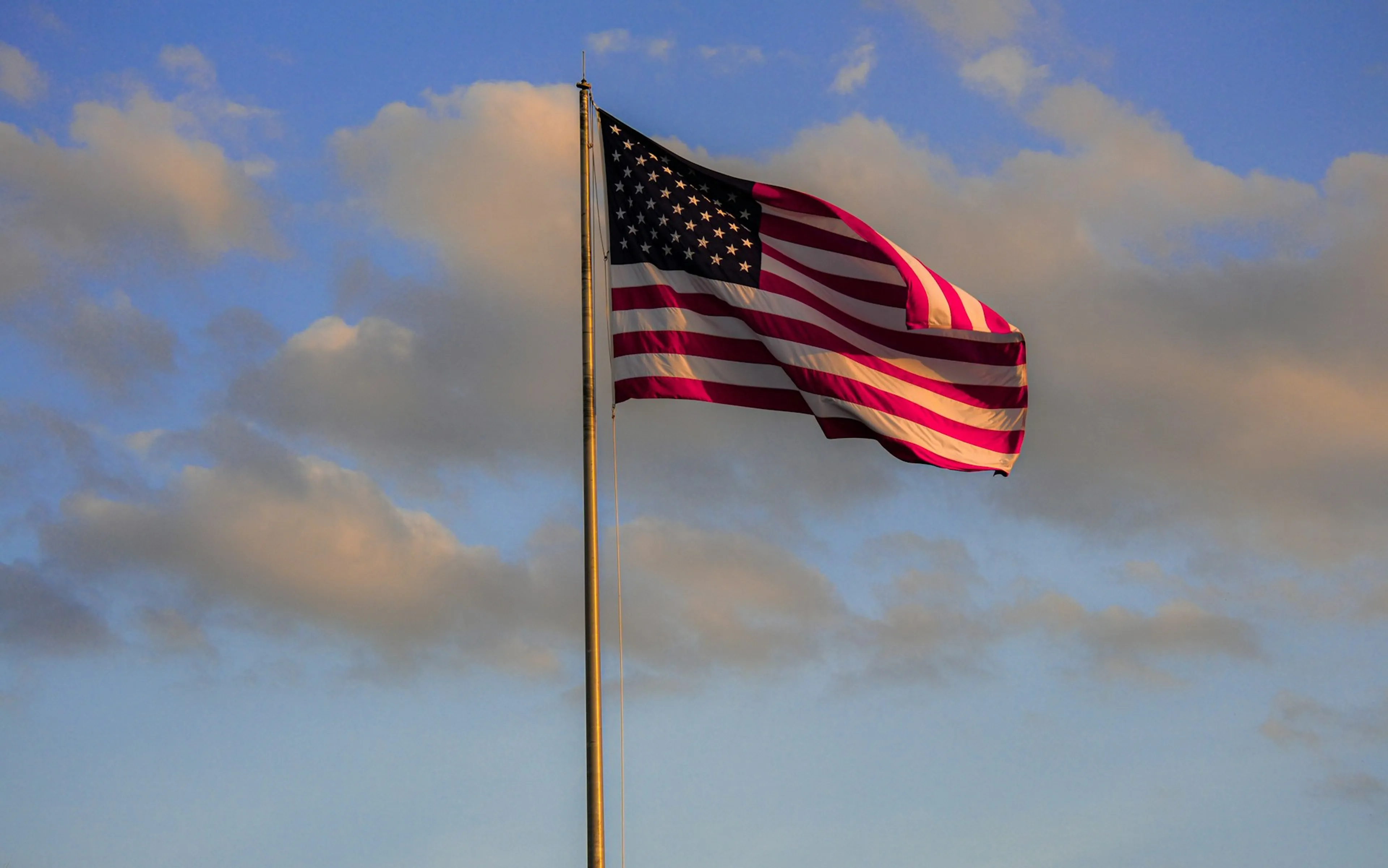 American flag waving against a blue sky with scattered clouds.