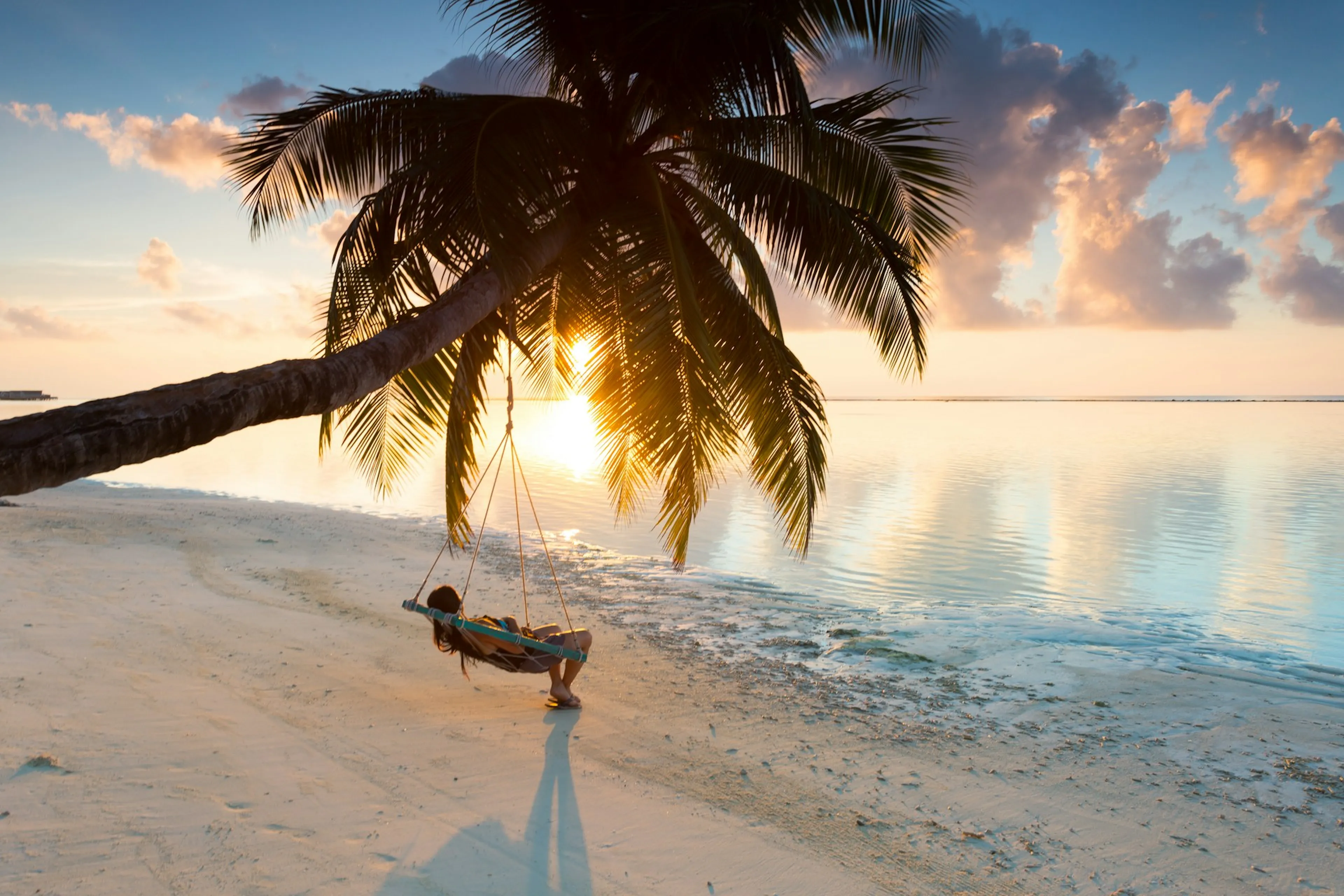 person lying in hammock on tropical beach at sunset