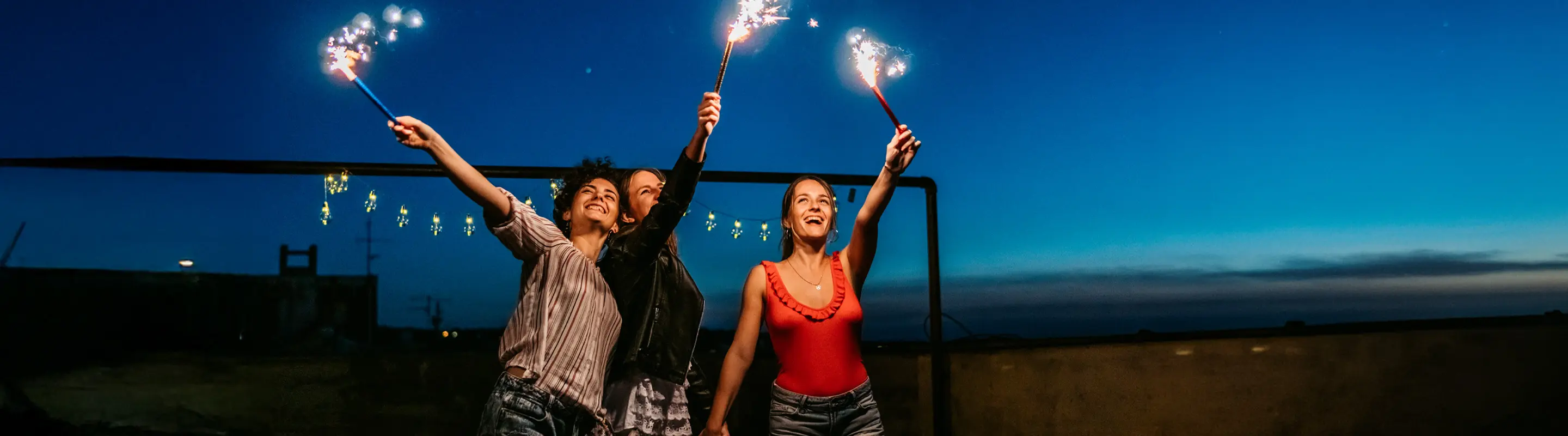 Three people joyfully hold sparklers against a twilight sky, creating a festive and celebratory atmosphere.