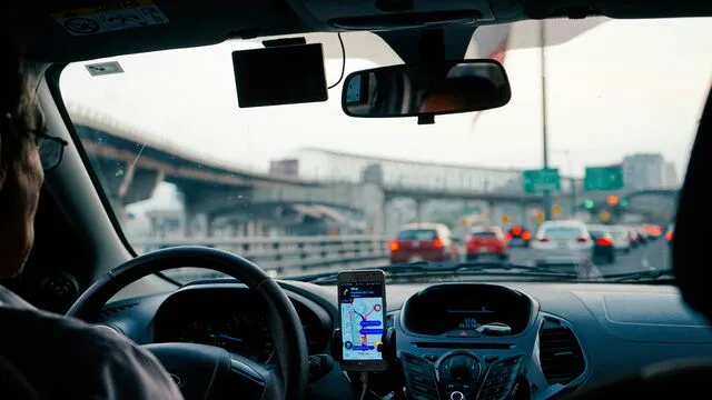 Driver's perspective in a car with a mounted GPS, navigating through traffic on a highway with a bridge ahead and multiple cars visible.