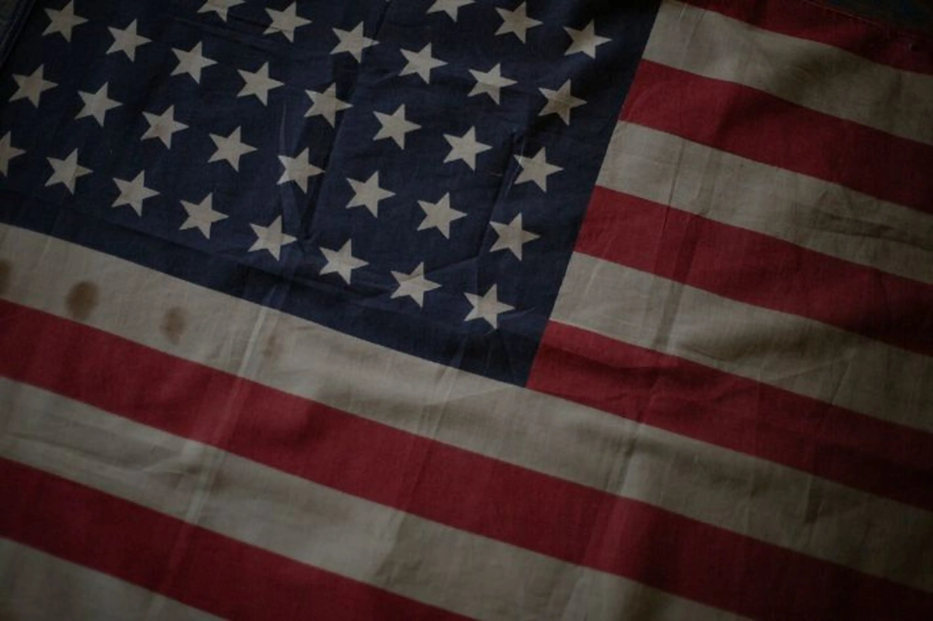 Worn American flag with visible creases and stains, displaying stars and red and white stripes.