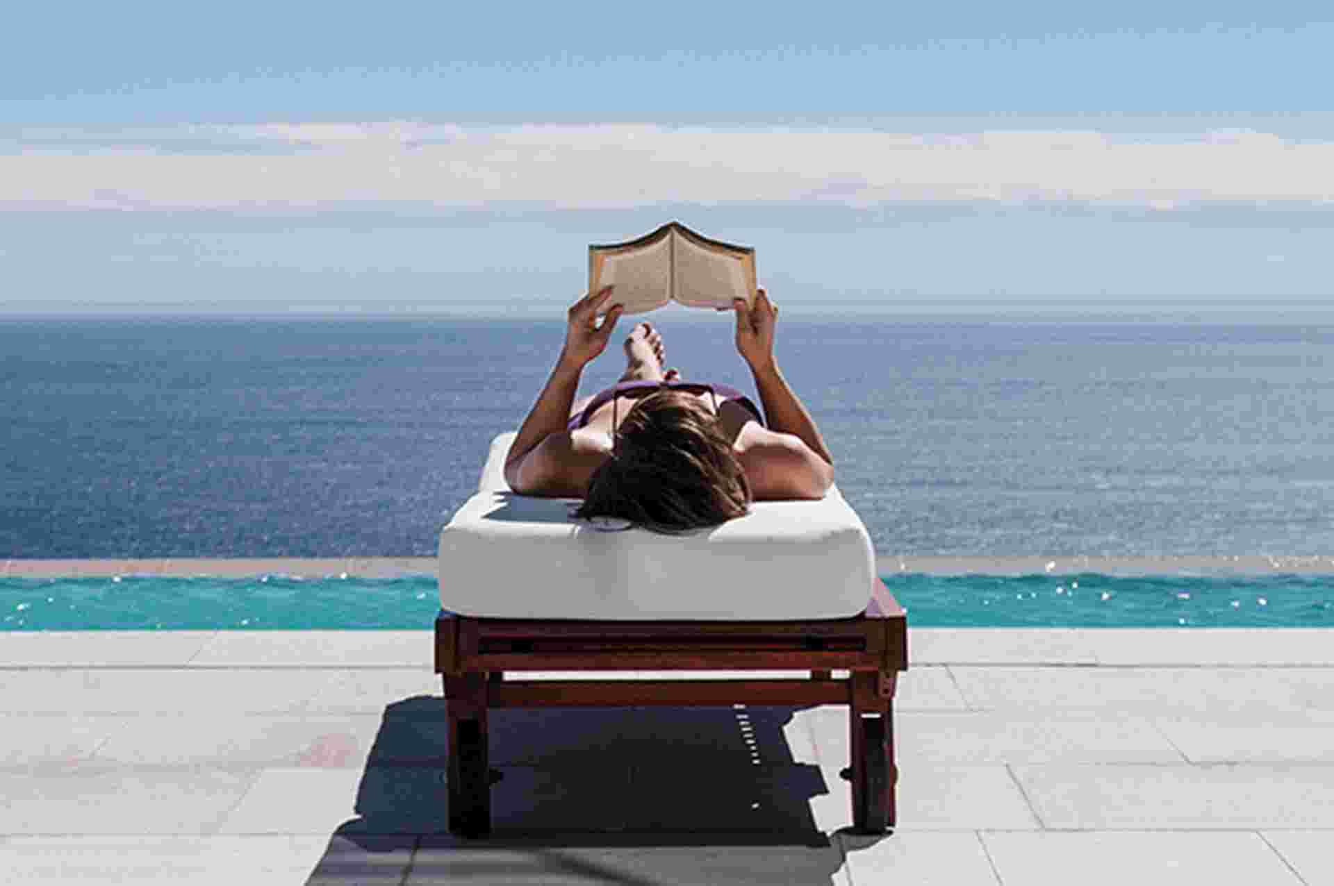 Woman relaxing on lounge chair at poolside overlooking ocean