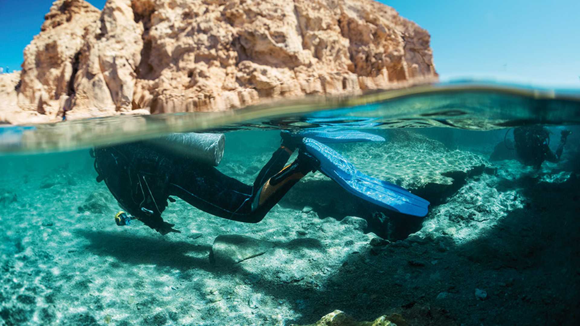 Split shot with diver underwater and rocky land of the Ras Muhammad National Park, Red Sea, Egypt