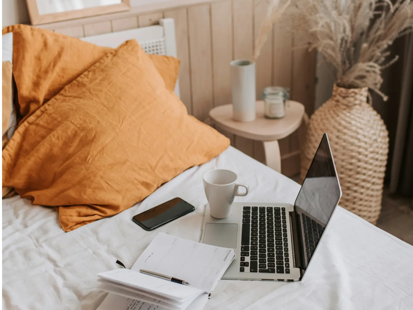 Hotel room setup with a laptop, notebook, phone and coffee cup on the bed