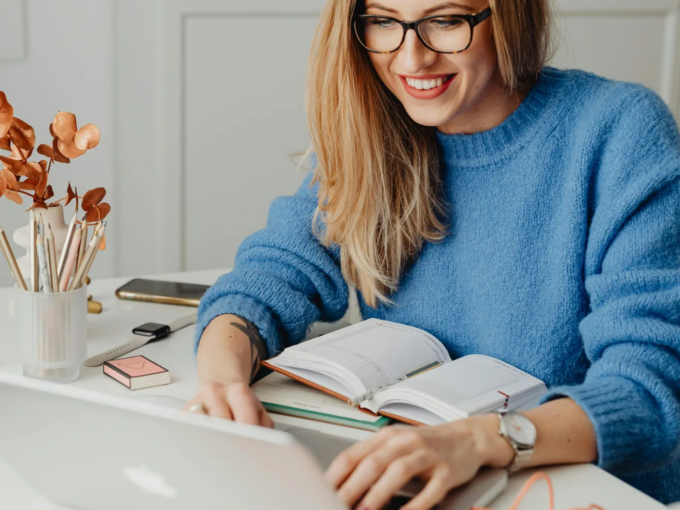Smiling hotel owner types on a laptop at a desk with an open notebook