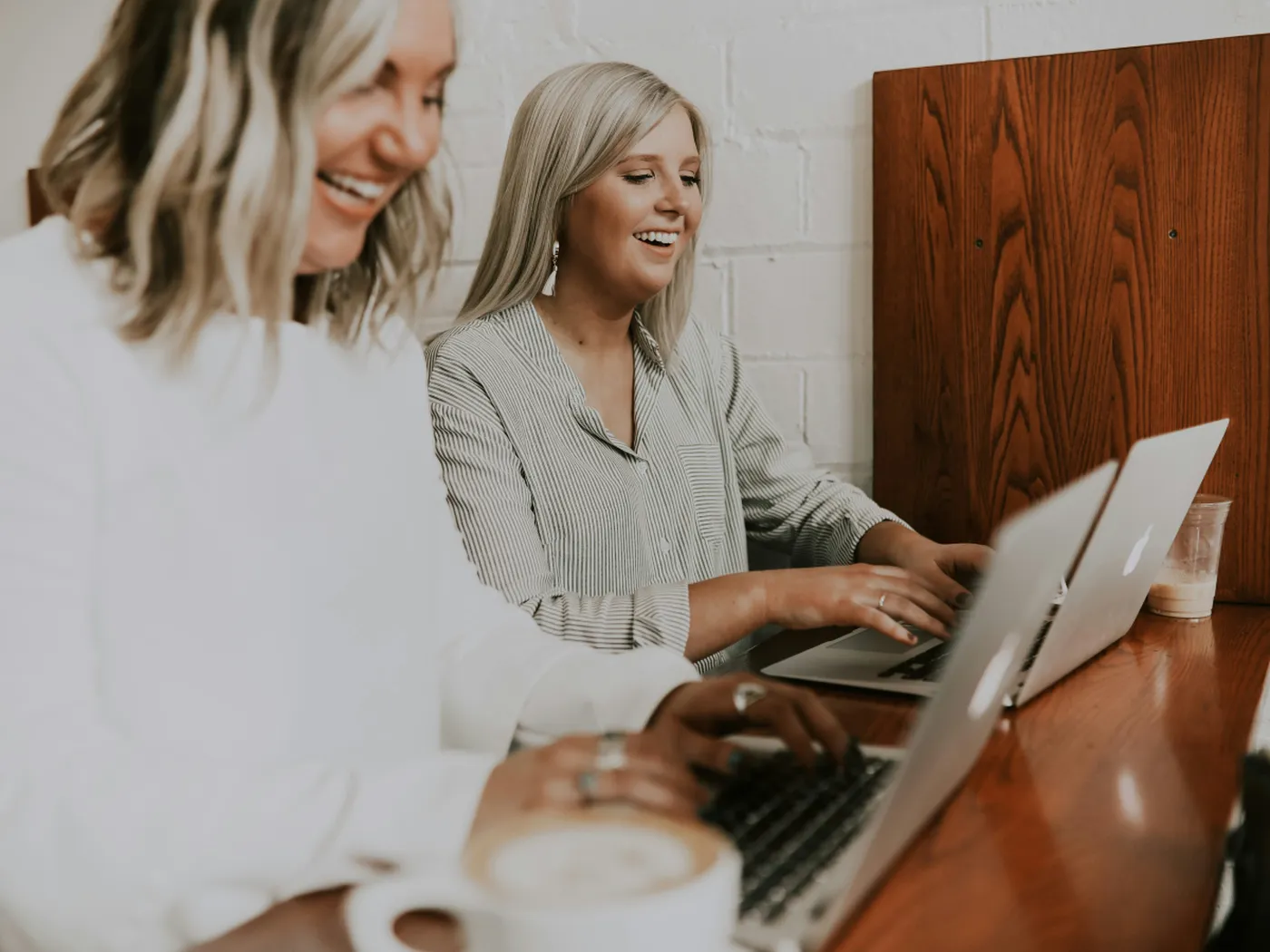 Two women smiling and working on laptops at a hotel reception desk