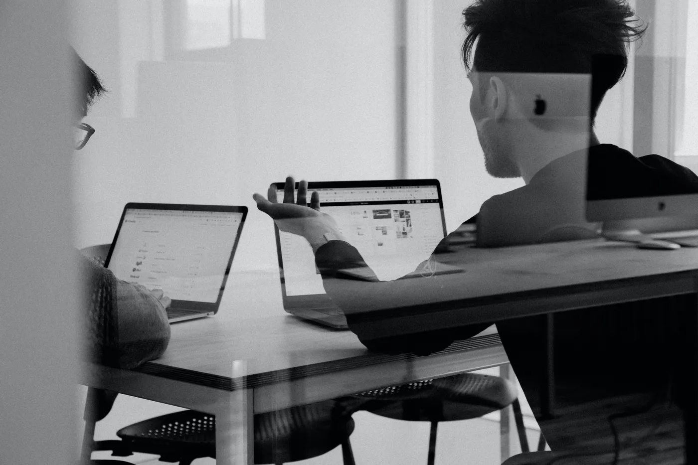 Two people sitting at a table with laptops, discussing work