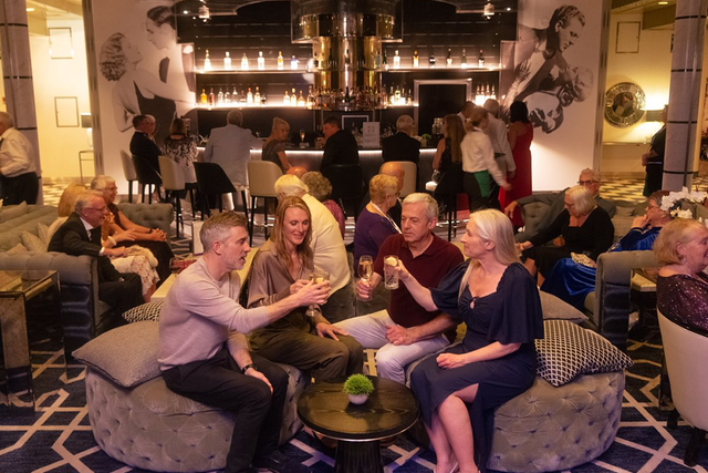 A group of people sitting in a Raffles lounge bar, toasting with drinks.
