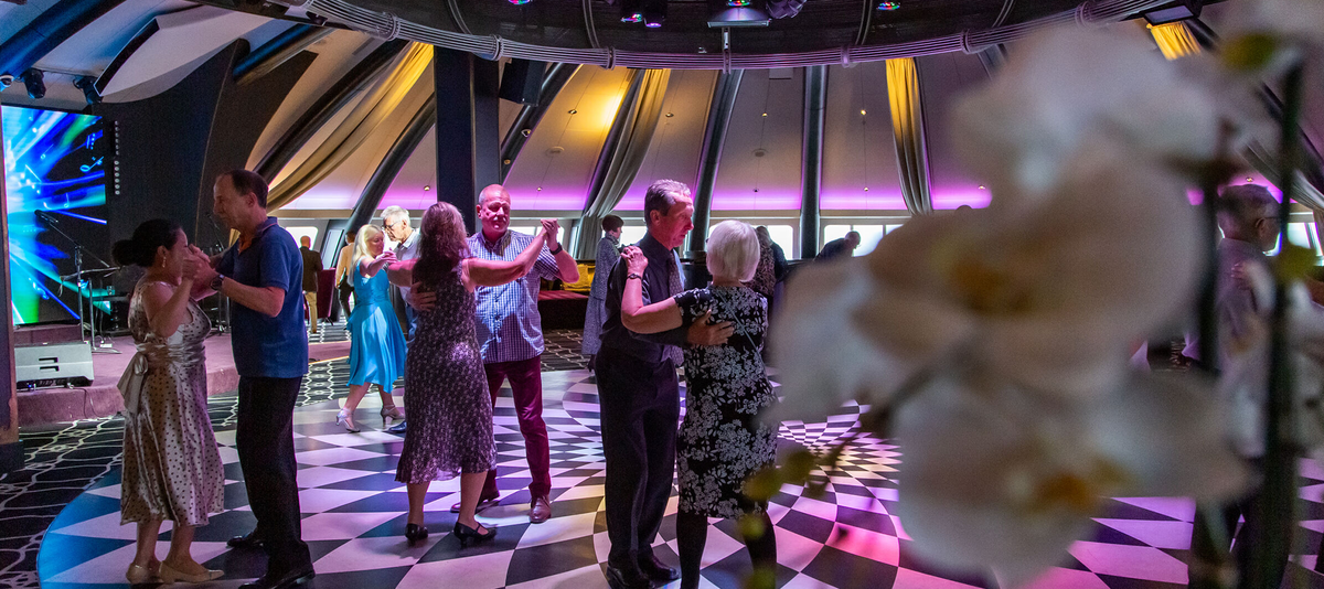Couples dancing on the dance floor in a dimly lit, stylish room with colorful lighting.