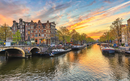 Sunset over an Amsterdam canal with boats and buildings lining the water, and a dramatic sky with vibrant clouds in Amsterdam, Netherlands.