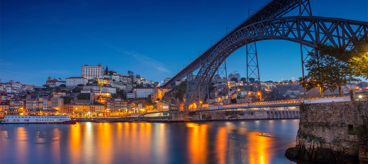 Illuminated bridge spanning a calm river at dusk, with city lights reflecting on the water in Porto, Portugal