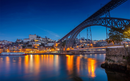 Illuminated bridge spanning a calm river at dusk, with city lights reflecting on the water in Porto, Portugal
