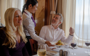 A smiling waiter serves a dish to a man at the Buckingham restaurant. A woman with long blonde hair is sitting beside him.