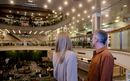 A man and woman overlook the spacious, Centre Court , surrounded by seating, and lit with numerous ceiling lights.