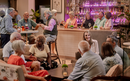 A group of guests socializing at the botanical bar, engaging in conversation, with drinks on tables and a vibrant, illuminated backdrop.