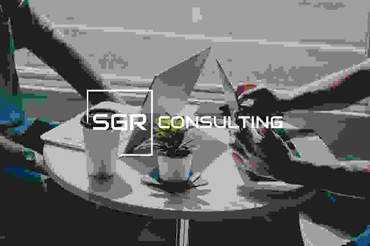 A coffee table with two laptops, a coffee cup, a notepad and a succulent on top of coasters with two people behind the computers.