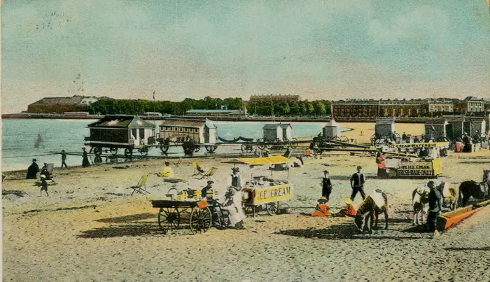 A view of Weymouth beach in Victorian times, with bathing huts and an ice cream stand