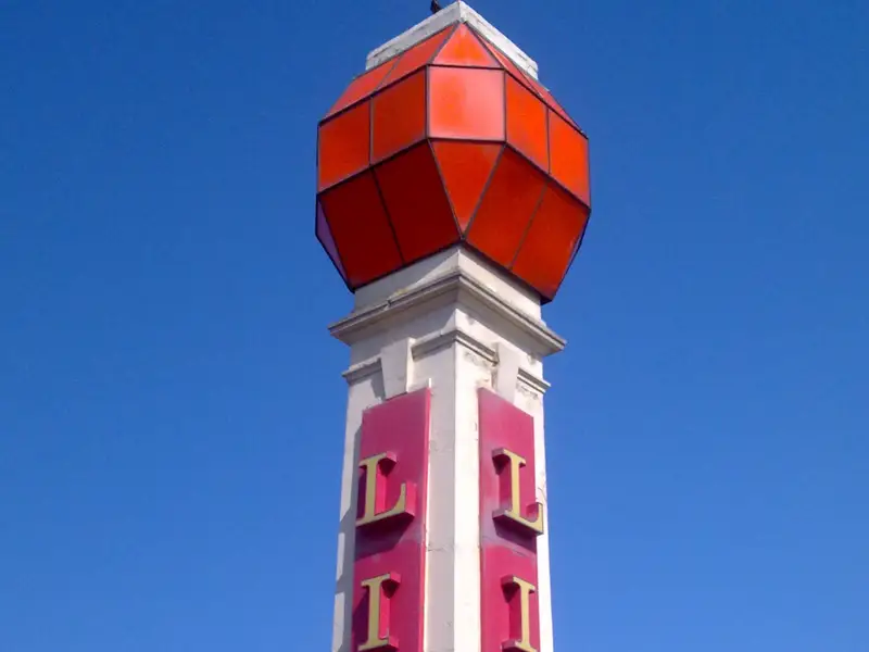 A tall, white column with red panels spelling "LIDO" vertically on both sides, topped with a red geometric structure against a clear blue sky.