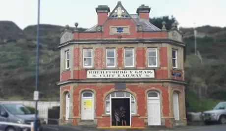 Historic red-brick railway building, labeled "Rhielffordd y Graig Cliff Railway," with arched windows and doors, set against a hillside.