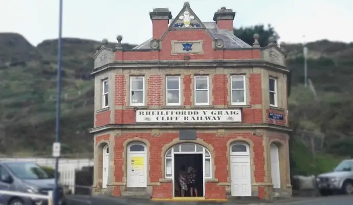 Historic red-brick railway building, labeled "Rhielffordd y Graig Cliff Railway," with arched windows and doors, set against a hillside.