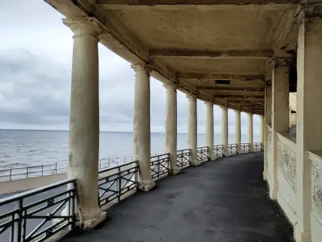 Seaside promenade with a series of stone columns and an overcast sky, offering a view of the ocean.