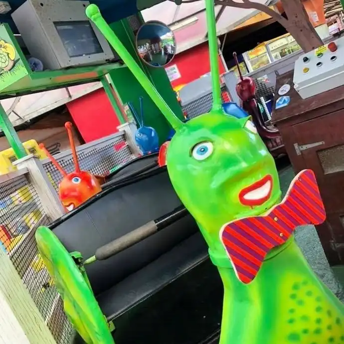 Colorful amusement park ride featuring a smiling green snail with a red bow tie and antennae. Bright and playful setting.