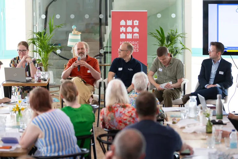 A panel of five people speaking at a conference, with a banner reading "Historic Buildings & Places" behind them, and an audience in the foreground.