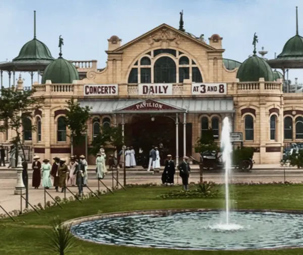 Historic pavilion hosting daily concerts at 3 and 8, with people in period attire walking nearby and a fountain in the foreground.
