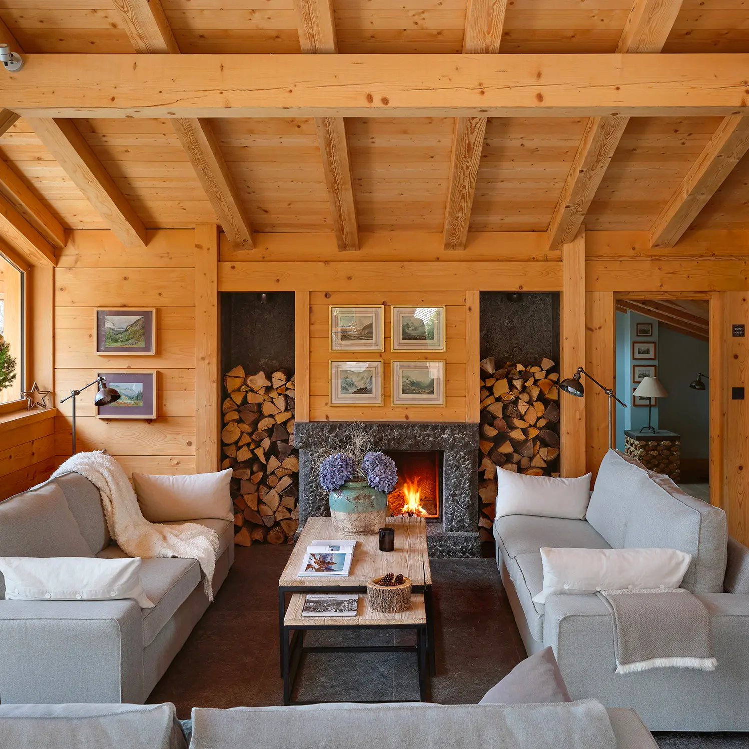 Location de Chalets Chamonix - Chalet Granit Les Rives d'Argentière - salon avec cheminée centrale en pierre et bûchers