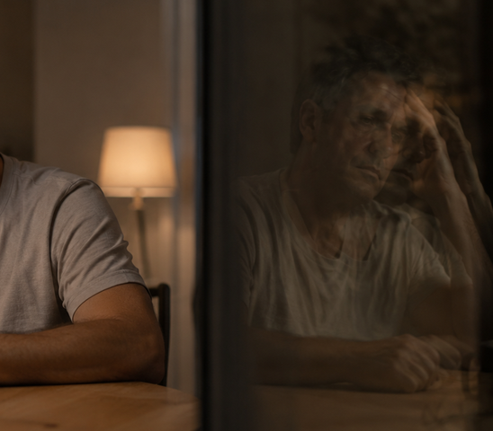 Man resting his head in his hand at night, reflected in a dark window