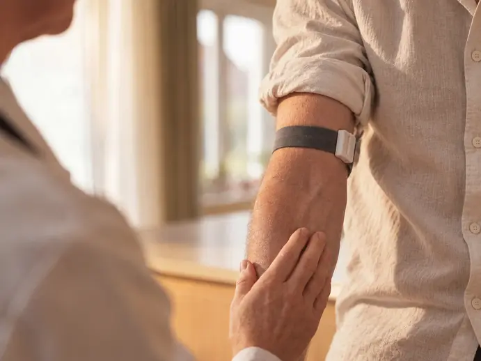 Hand einer Fachperson am Arm eines Patienten mit angelegtem Stauband