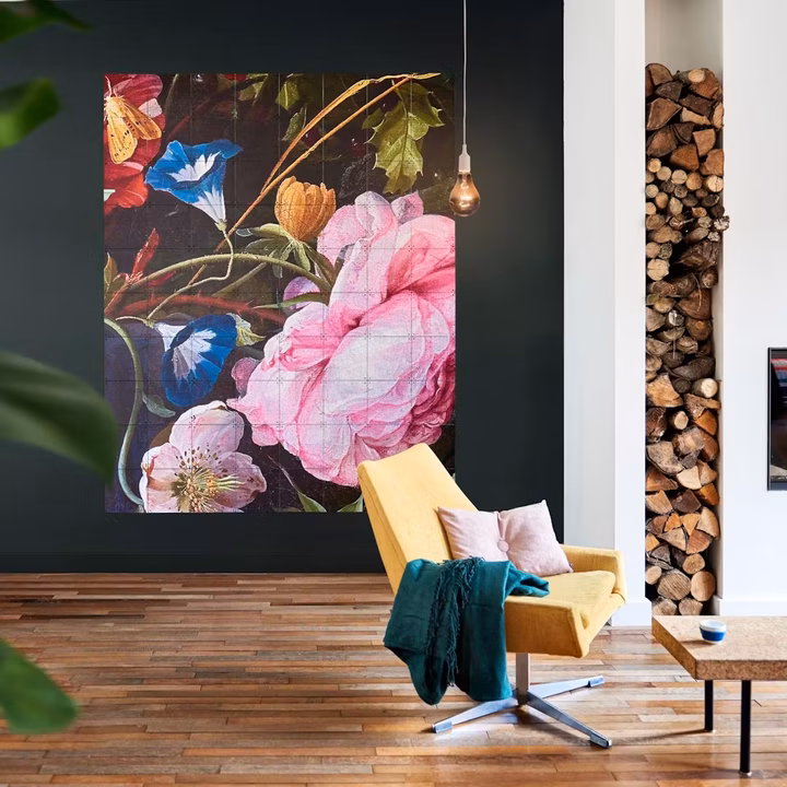 The same still life zoomed in on a single pink rose, large on a dark wall beside a yellow armchair
