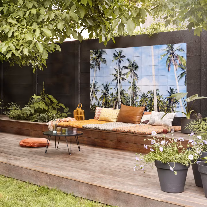 Large IXXI of palm trees on a dark garden wall, above a bench on a terrace under a tree